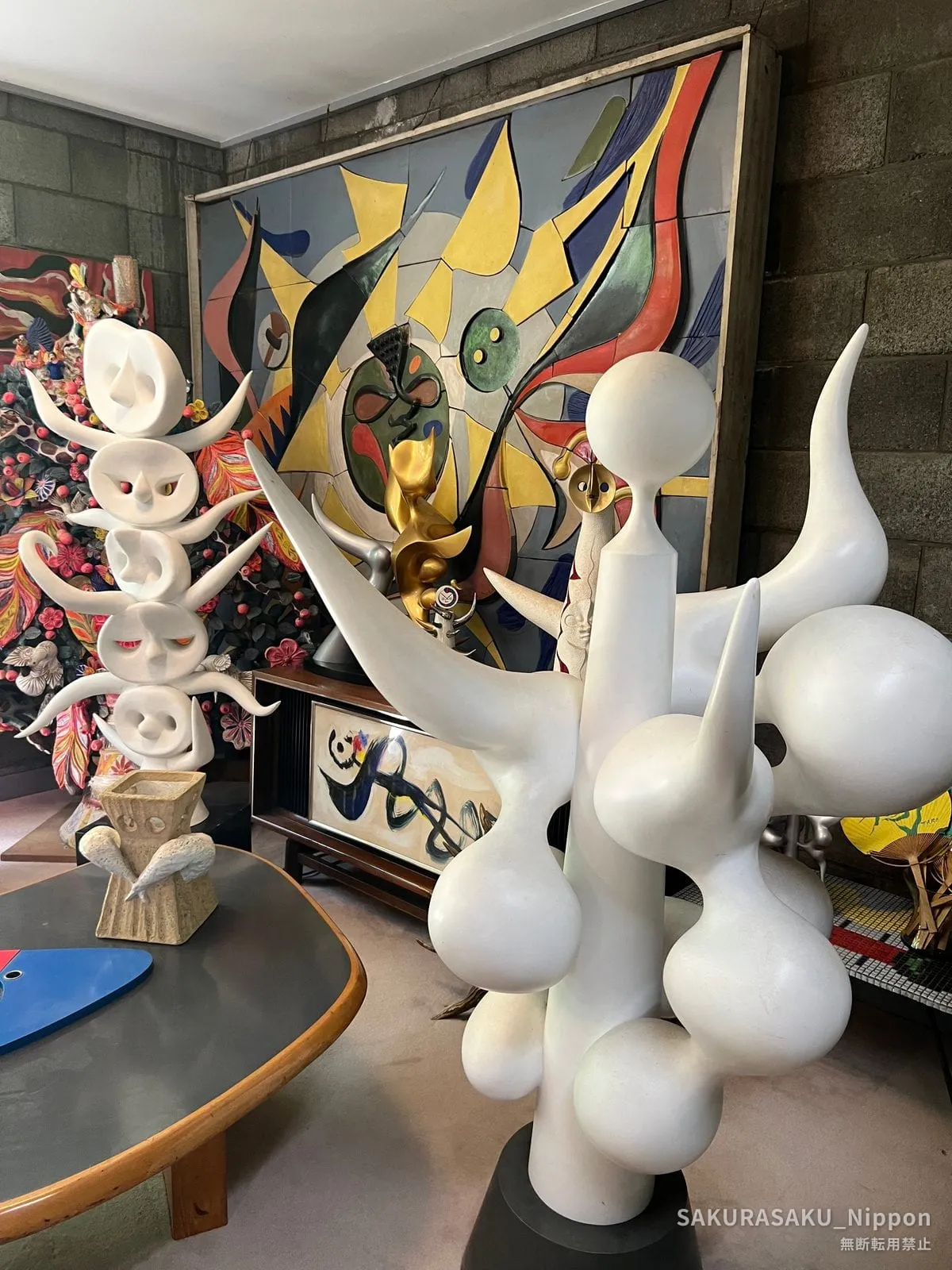 White abstract sculptures crowded together in the museum garden, in front of a coloured tile mural