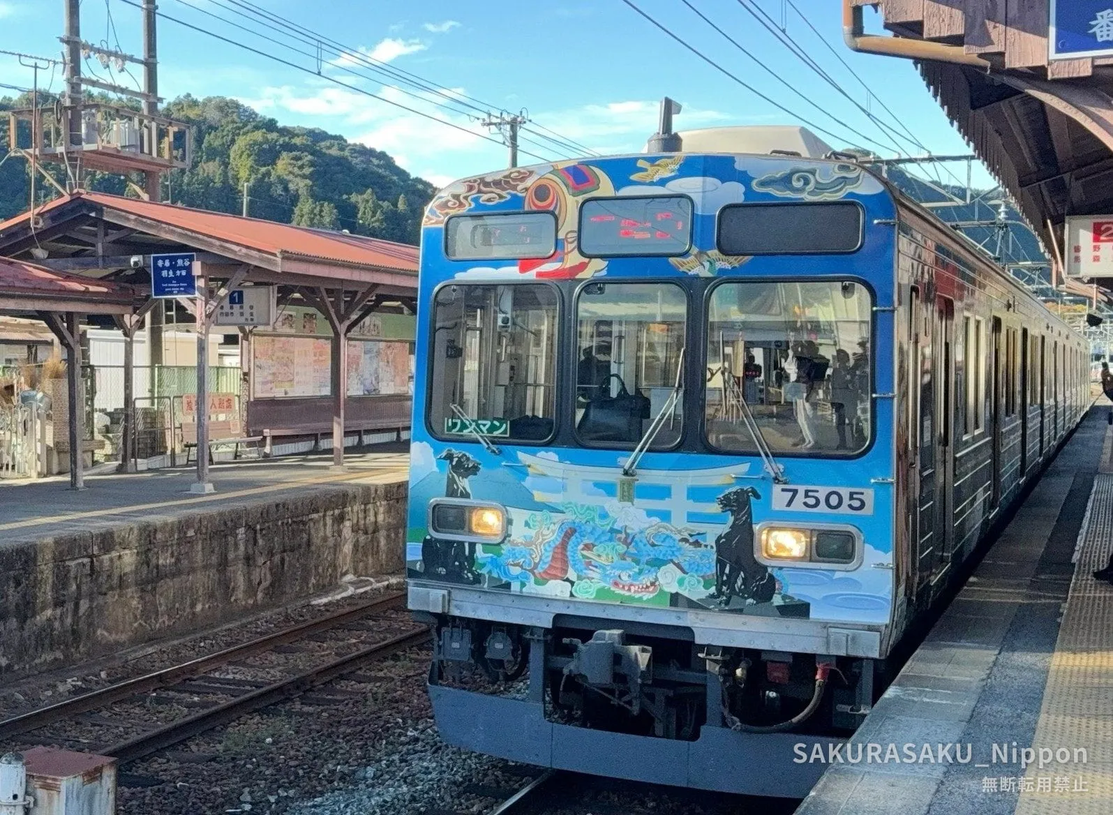 A wrapped Chichibu Railway 7500 series train at a country platform, painted with dragons and black wolves