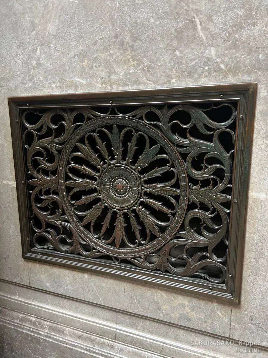 A bronze ventilation grille, cast in leaves and scrolls, set into a marble wall