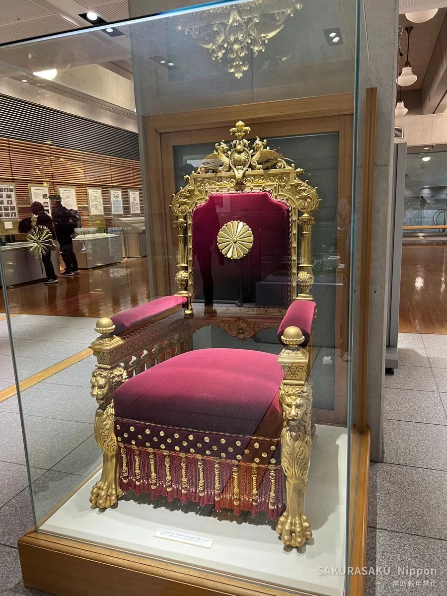 The gilded ceremonial chair, upholstered in crimson and bearing the chrysanthemum crest