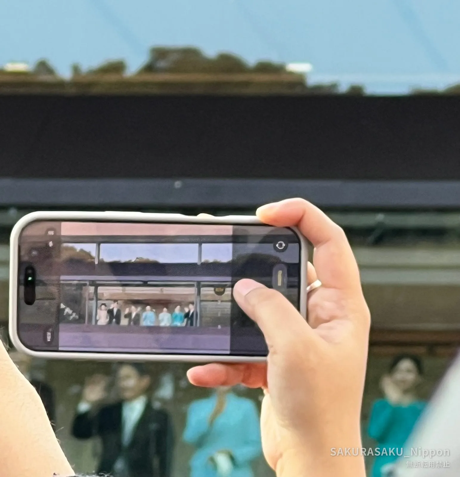 Watching the balcony through a phone screen, among the crowd