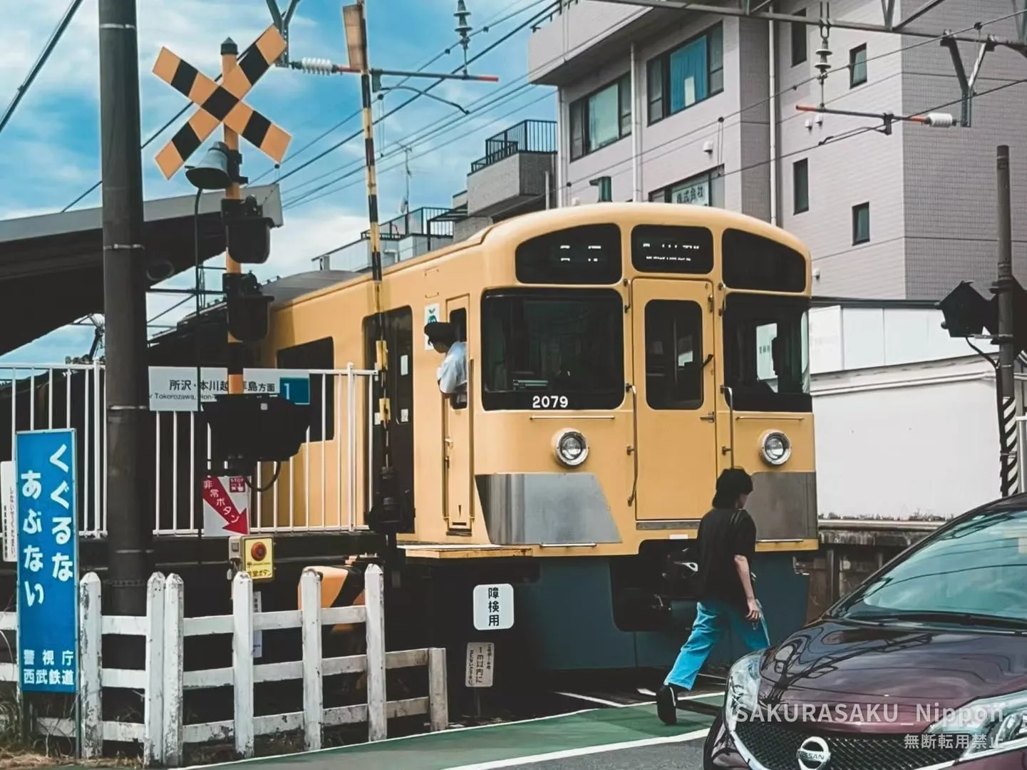 A yellow Seibu train stopped at the Kami-Igusa level crossing, its nose reaching almost to where people cross