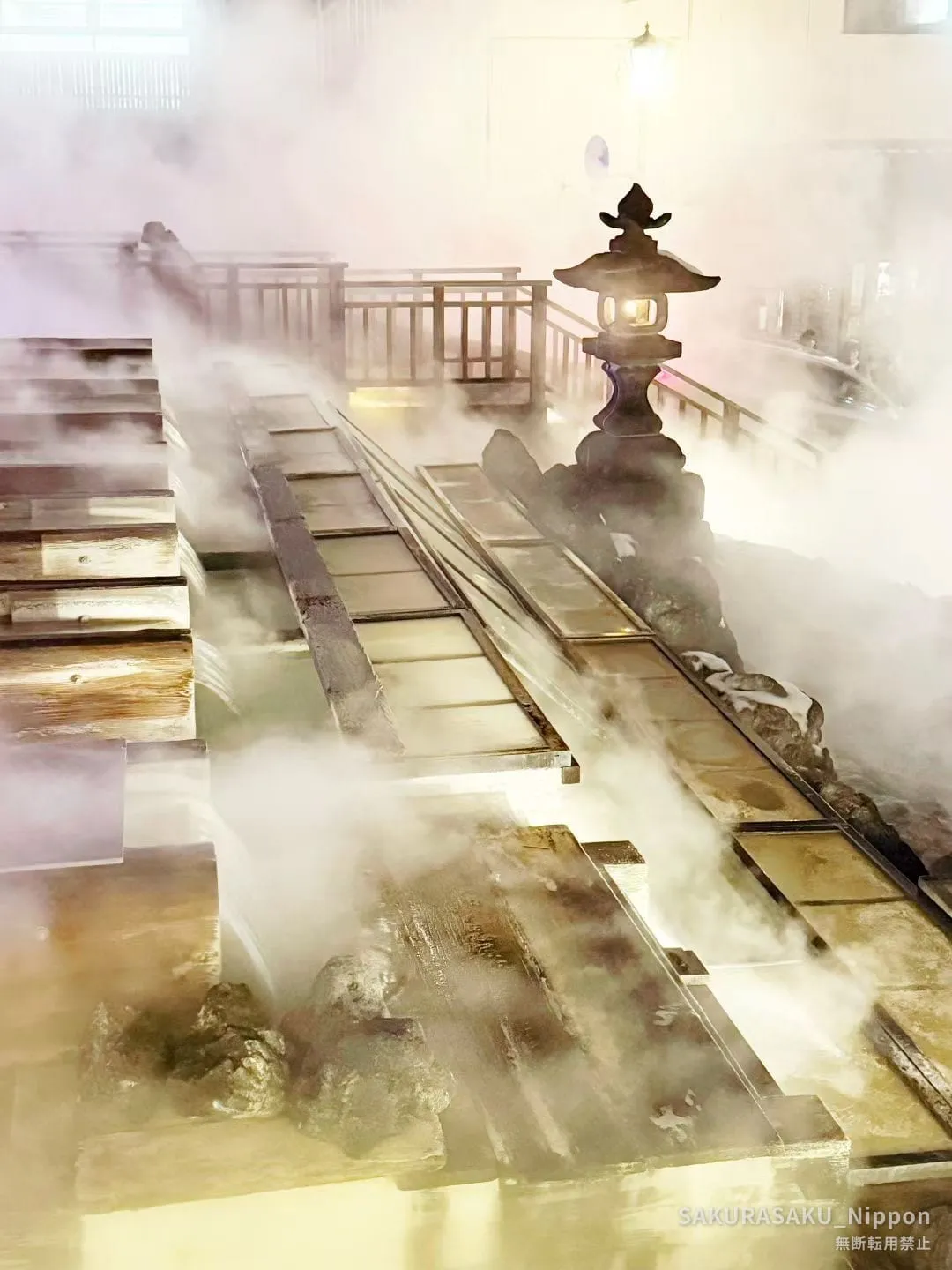 Steam rising from the yubatake channels around the stone lantern