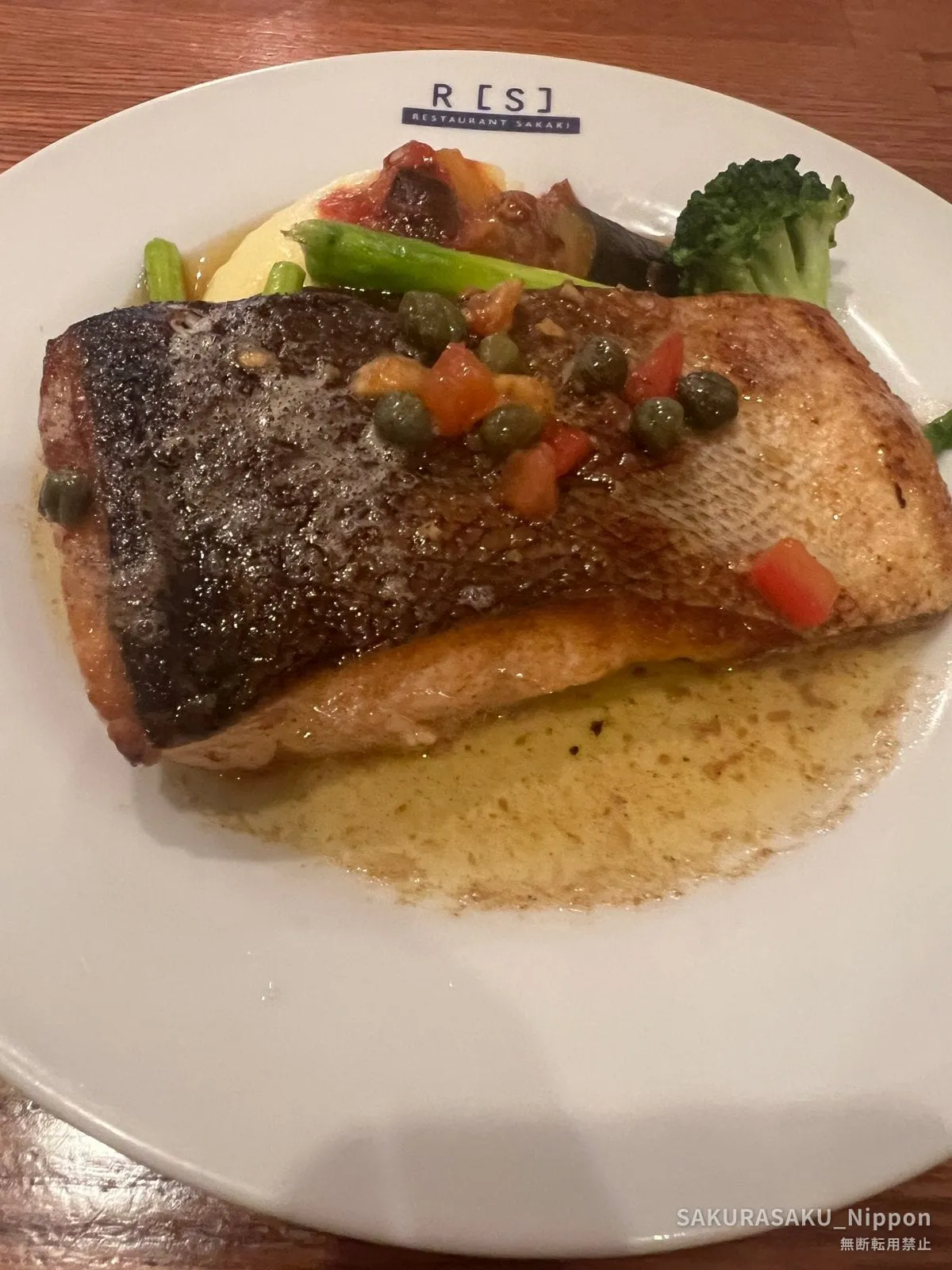 Pan-seared fish with tomato, olive and caper sauce on a plate marked R[S] Restaurant SAKAKI