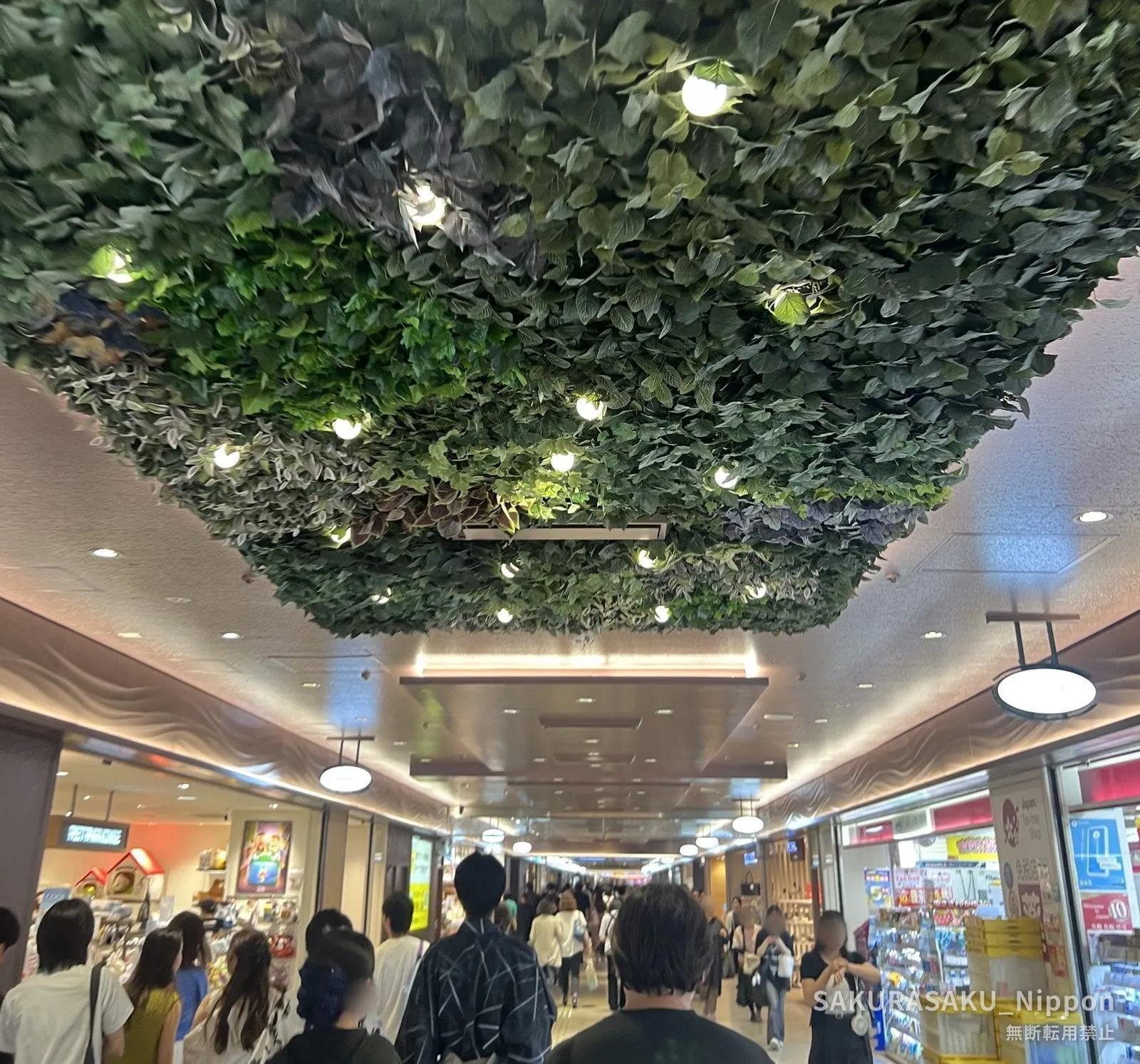 A shopping street under Shinjuku, its ceiling covered in a canopy of green foliage, with people walking between shops