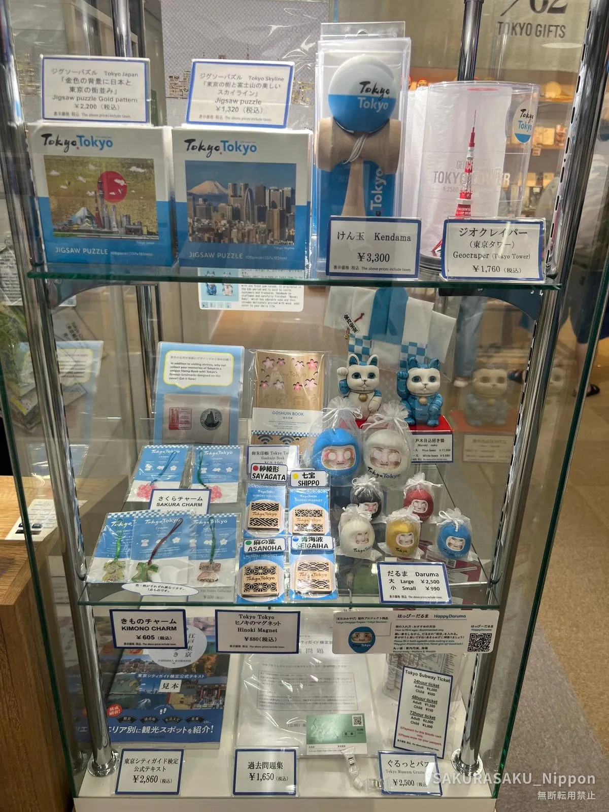 A display case of Tokyo souvenirs — jigsaw puzzles, a kendama, daruma dolls and kimono charms