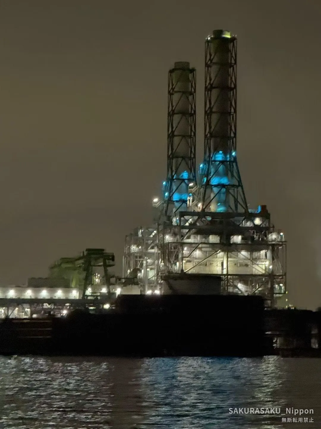 A tall industrial structure lit in blue and white on the far bank of the canal at night