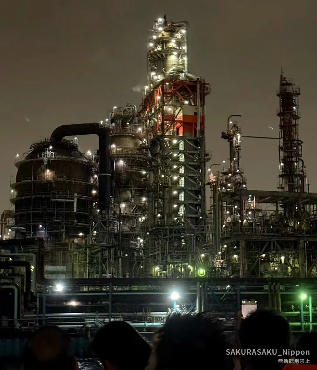 A refinery packed with pipework and towers, lit from below, seen from the canal at night